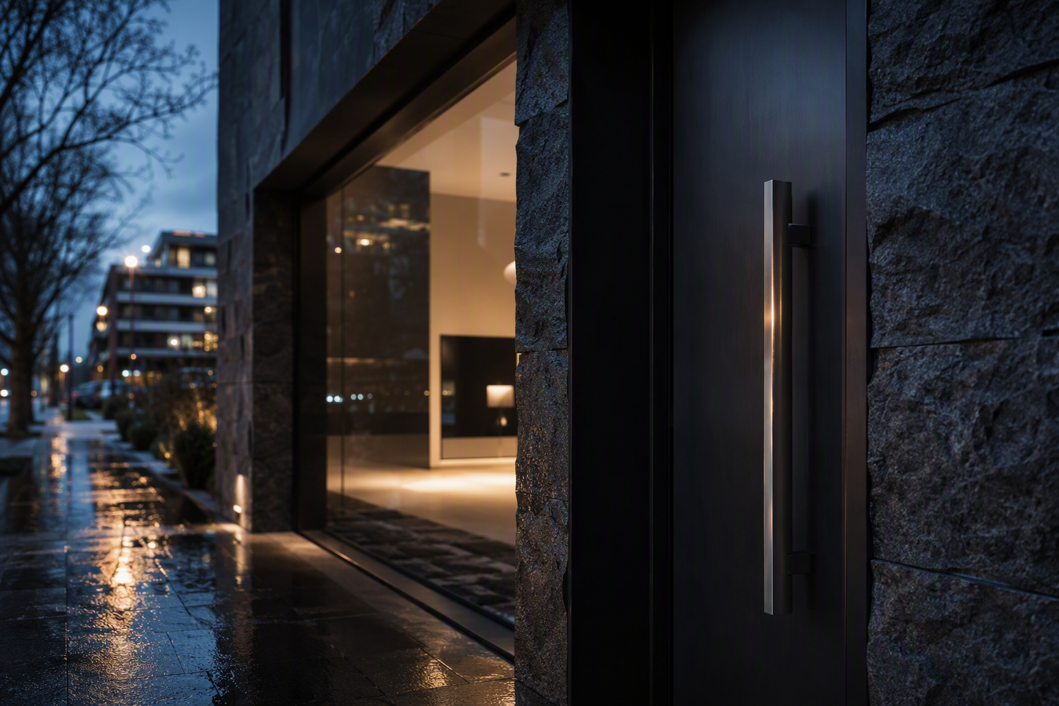 Recessed bluestone and blackened steel entrance to a modern Melbourne apartment building at dusk, with brushed stainless door hardware lit from above.