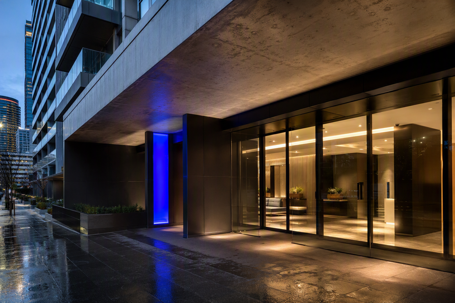 Contemporary Melbourne apartment and office entry at dusk, with dark anodised portal, concrete soffit and warm lobby light on wet pavement