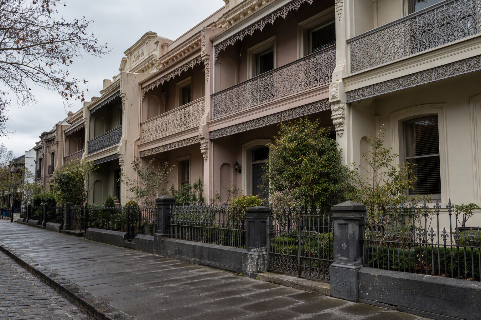 Row of Victorian terrace houses with cast-iron lace verandahs and low iron front gates on a bluestone street