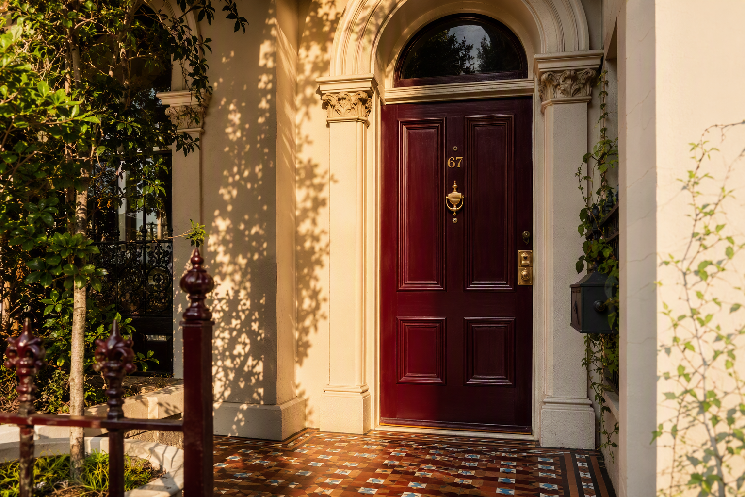 Deep burgundy panelled timber front door with aged brass numerals and a rim lock in a rendered archway