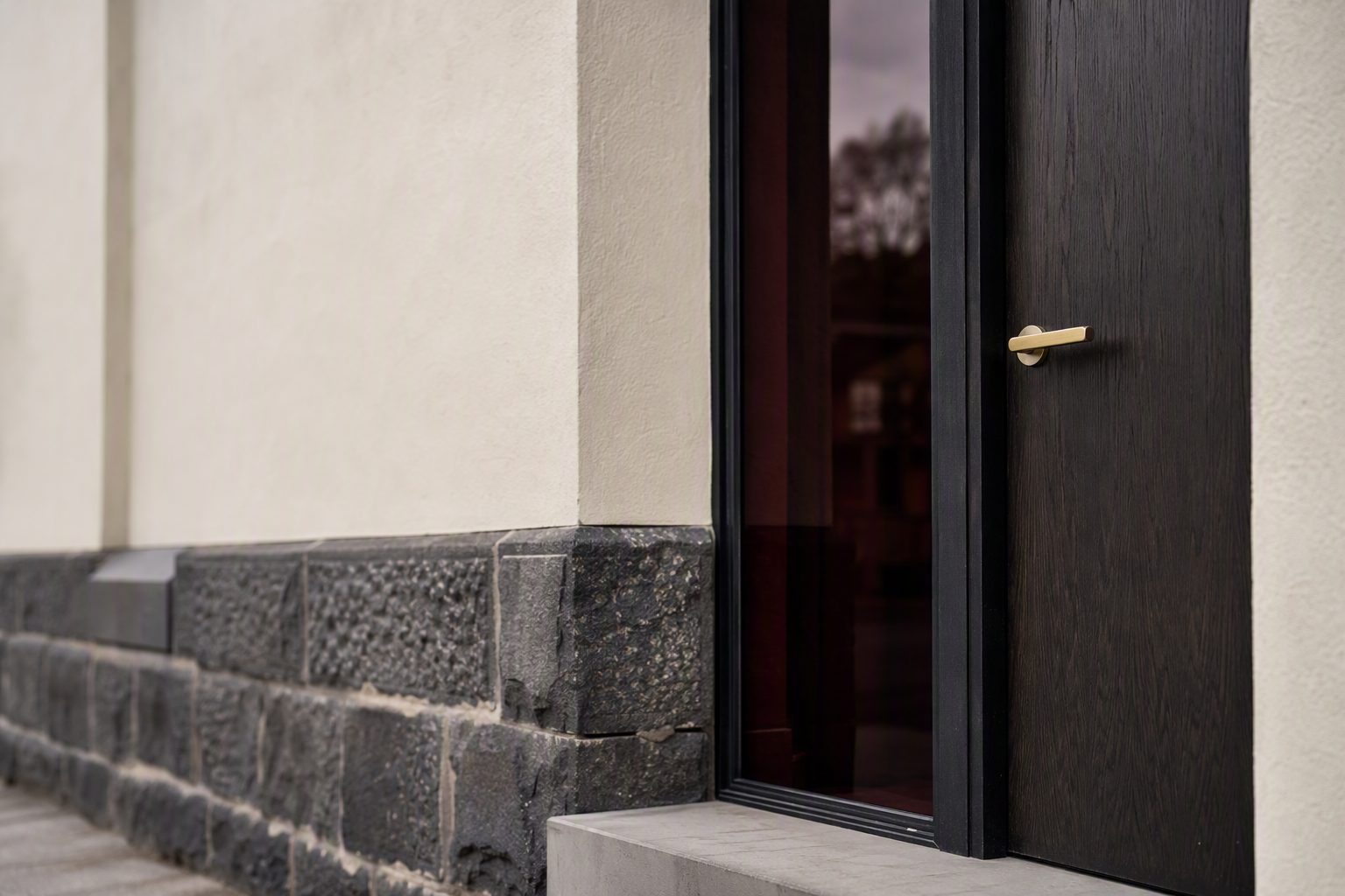 Dark timber front door with a slim brushed brass lever handle set into a rendered heritage facade, photographed off-centre