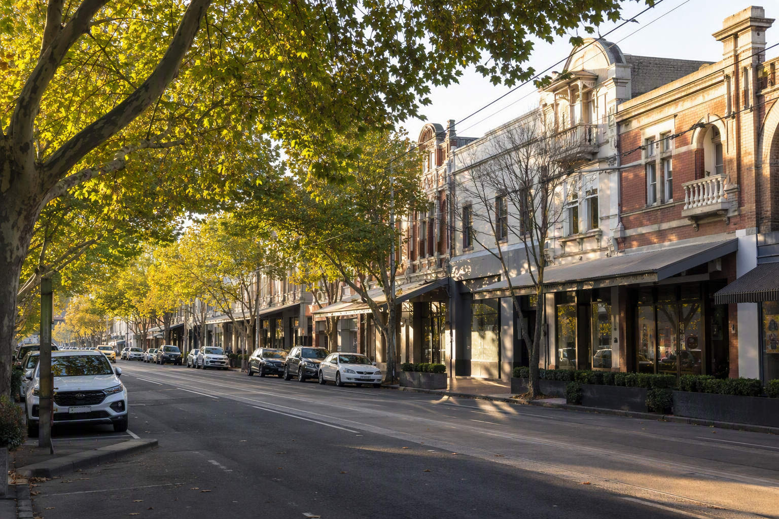 Leafy Melbourne shopping strip with heritage brick retail buildings, awnings and mature street trees
