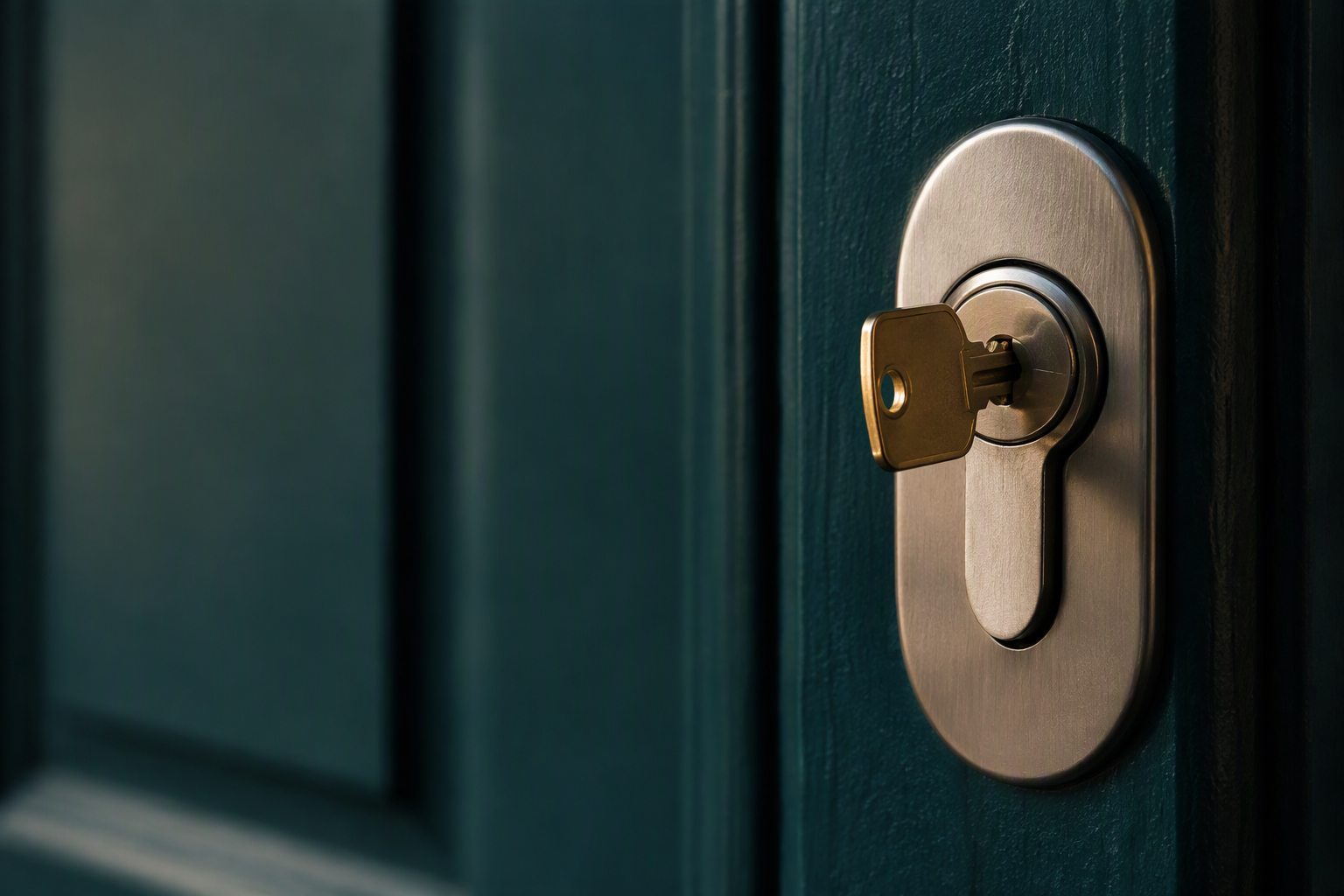 Close-up of a brushed steel lock cylinder with a brass key in a petrol-green front door