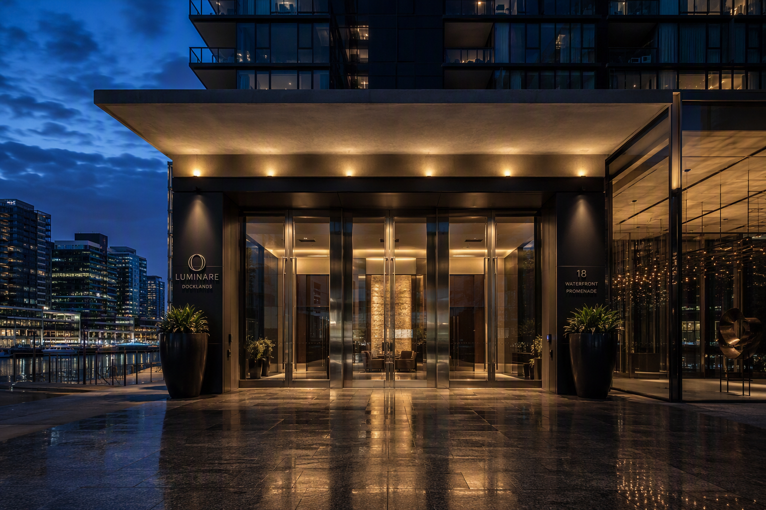 Modern Docklands apartment tower entrance with glass and brushed metal doors lit at blue hour